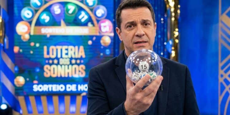 Homem de terno segura globo transparente com bola número 15 em estúdio da Loteria dos Sonhos