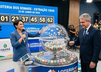 Apresentadora e homem em sorteio da Loteria dos Sonhos, atrás de globo com bolas numeradas, painel azul ao fundo