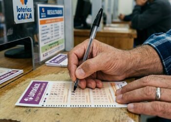 Homem marca volante da Lotofácil com caneta próximo ao balcão de uma lotérica Caixa