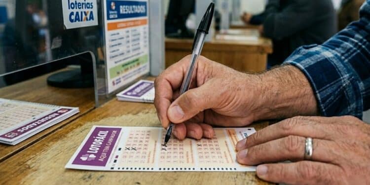 Homem marca volante da Lotofácil com caneta próximo ao balcão de uma lotérica Caixa