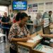 Pessoas preenchem apostas na lotérica com fila e atendente da Caixa orientando sobre o sorteio Mega-Sena 3022