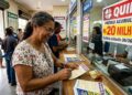 Mulher preenche bilhete da Quina em lotérica, cartaz anuncia prêmio de 20 milhões