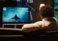 Homem assistindo televisão digital em sala moderna com foco em transmissão de canais comerciais e educativos.