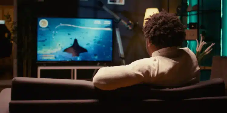Homem assistindo televisão digital em sala moderna com foco em transmissão de canais comerciais e educativos.