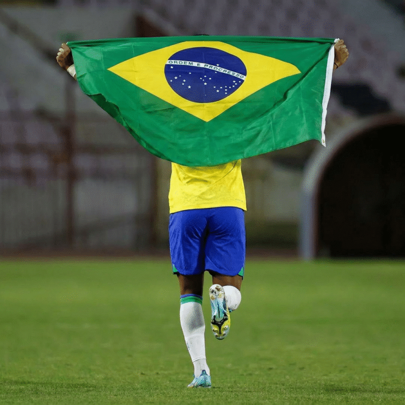 Jogador exibindo bandeira do Brasil em campo.