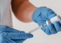 Profissional de saúde prepara seringa com vacina em ambiente clínico.
