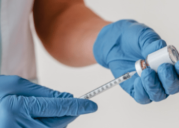 Profissional de saúde prepara seringa com vacina em ambiente clínico.