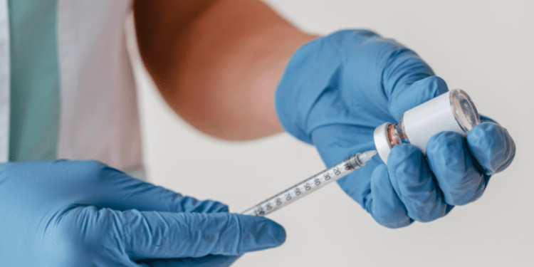 Profissional de saúde prepara seringa com vacina em ambiente clínico.