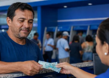 Trabalhador recebendo cédulas de real em agência bancária, representando o pagamento do Abono Salarial para casos de envio correto dos dados até 20 de junho.