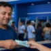 Trabalhador recebendo cédulas de real em agência bancária, representando o pagamento do Abono Salarial para casos de envio correto dos dados até 20 de junho.