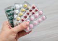 Cartelas de medicamentos seguradas por uma mão, ilustrando recolhimento de lotes pela Anvisa.