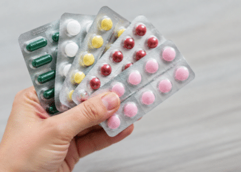Cartelas de medicamentos seguradas por uma mão, ilustrando recolhimento de lotes pela Anvisa.