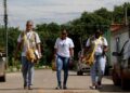 Três agentes de saúde caminham por uma rua com bolsas de trabalho a tiracolo durante visita de campo