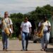 Três agentes de saúde caminham por uma rua com bolsas de trabalho a tiracolo durante visita de campo