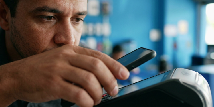 Homem aproxima o celular de uma maquininha para concluir um pagamento