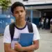 Adolescente em escola pública segurando caderno azul com expressão preocupada, representando a ausência dos pagamentos do Pé-de-Meia de junho para oito grupos.