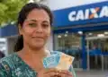 Beneficiária segura notas de real em frente a uma agência da Caixa, representando o pagamento do Bolsa Família.