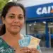 Beneficiária segura notas de real em frente a uma agência da Caixa, representando o pagamento do Bolsa Família.