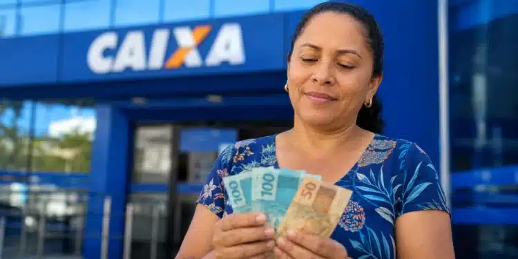 Mulher segura cédulas de reais em frente a uma agência da Caixa, representando o último repasse de junho do Bolsa Família.