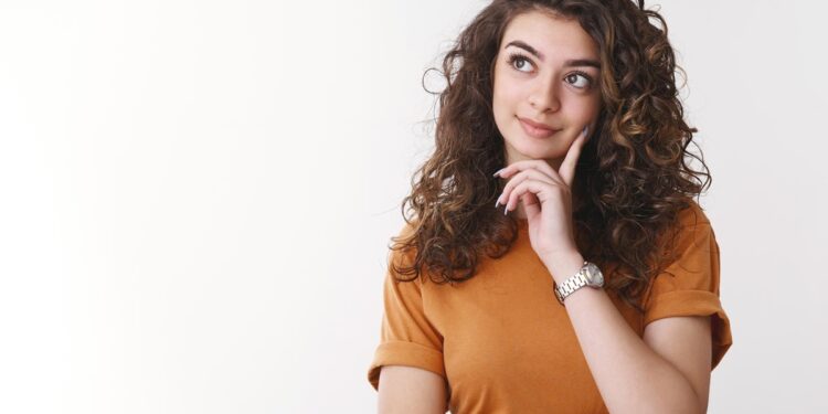 Mulher com expressão pensativa, a mão no rosto, olhando para o lado em fundo claro