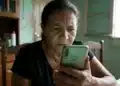 Mulher segurando celular em casa enquanto consulta mensagem relacionada ao BPC enviada pelo INSS via WhatsApp.