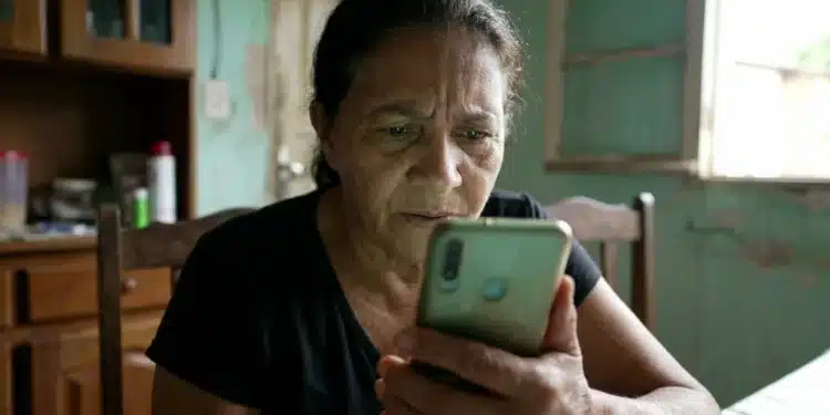 Mulher segurando celular em casa enquanto consulta mensagem relacionada ao BPC enviada pelo INSS via WhatsApp.