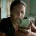Mulher segurando celular em casa enquanto consulta mensagem relacionada ao BPC enviada pelo INSS via WhatsApp.