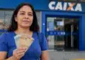 Mulher segurando cédulas de dinheiro em frente a uma agência da Caixa, representando depósitos de R$ 600, R$ 800 e R$ 1.000.