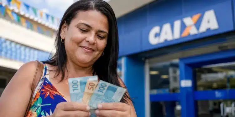 Mulher segura cédulas de dinheiro em frente a uma agência da Caixa, em referência à liberação de R$ 800 e R$ 1.000 no São João.