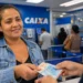 Mulher recebendo dinheiro em agência da Caixa, representando o pagamento de até R$ 1.000 para milhões de famílias brasileiras.