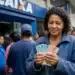 Mulher segura notas de real em frente à Caixa, representando o saque de até R$ 6.220 para CPFs com finais de 0 a 9