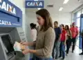Mulher retirando dinheiro em caixa eletrônico da Caixa, representando o pagamento de R$ 300 para CPFs com finais de 0 a 9 nesta segunda-feira (8).