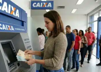 Mulher retirando dinheiro em caixa eletrônico da Caixa, representando o pagamento de R$ 300 para CPFs com finais de 0 a 9 nesta segunda-feira (8).