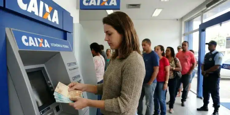 Mulher retirando dinheiro em caixa eletrônico da Caixa, representando o pagamento de R$ 300 para CPFs com finais de 0 a 9 nesta segunda-feira (8).
