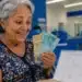 Aposentada sorrindo ao conferir cédulas de real em ambiente bancário, com calendário desfocado, ilustrando o pagamento do INSS de junho.