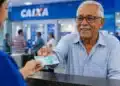 Idoso sorridente recebe dinheiro em atendimento bancário na Caixa, representando o pagamento de R$ 1.621 do INSS em junho.