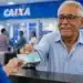Idoso sorridente recebe dinheiro em atendimento bancário na Caixa, representando o pagamento de R$ 1.621 do INSS em junho.