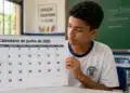 Estudante em sala de aula segurando calendário de junho de 2026, representando o cronograma de pagamentos do Pé-de-Meia deste mês.