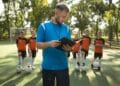 Treinador com prancheta orienta time de jovens jogadores de futebol em campo gramado