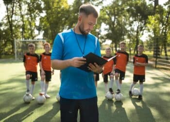 Treinador com prancheta orienta time de jovens jogadores de futebol em campo gramado