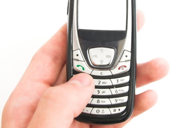 Mão segura celular antigo com teclado numérico e tela pequena