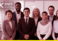 Equipe de profissionais sorridentes posa em ambiente corporativo ao lado da logomarca da Rede Nacional de Certificadores do Enem