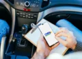 Candidato consulta informações da CNH pelo celular dentro de um carro durante processo de habilitação.