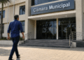 Homem caminhando em direção à entrada da Câmara Municipal em área urbana durante o dia.