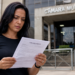 Mulher adulta lê edital de concurso público na entrada da Câmara Municipal, com expressão séria.