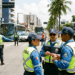 Quatro agentes de trânsito do DETRAN-AL com uniforme azul e colete amarelo, conversam em avenida de Maceió.