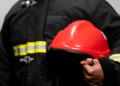 Bombeiro fardado segurando capacete vermelho durante divulgação de concurso dos Bombeiros de Alagoas.