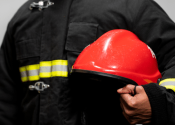 Bombeiro fardado segurando capacete vermelho durante divulgação de concurso dos Bombeiros de Alagoas.