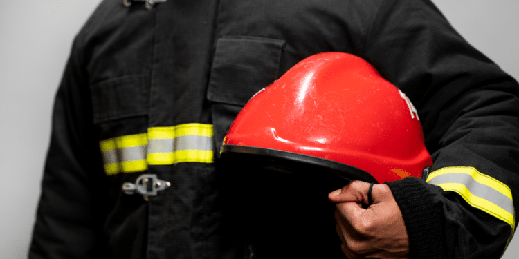 Bombeiro fardado segurando capacete vermelho durante divulgação de concurso dos Bombeiros de Alagoas.