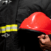 Bombeiro fardado segurando capacete vermelho durante divulgação de concurso dos Bombeiros de Alagoas.